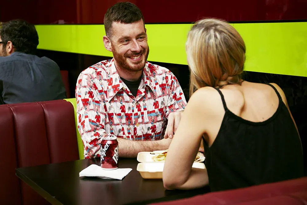 Two diners sharing a takeaway meal in a red booth at Topkapi Takeaway & Cafe