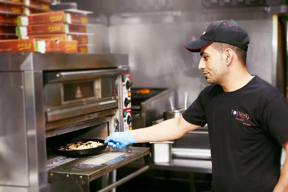 A Topkapi chef taking a dish out of the pizza oven